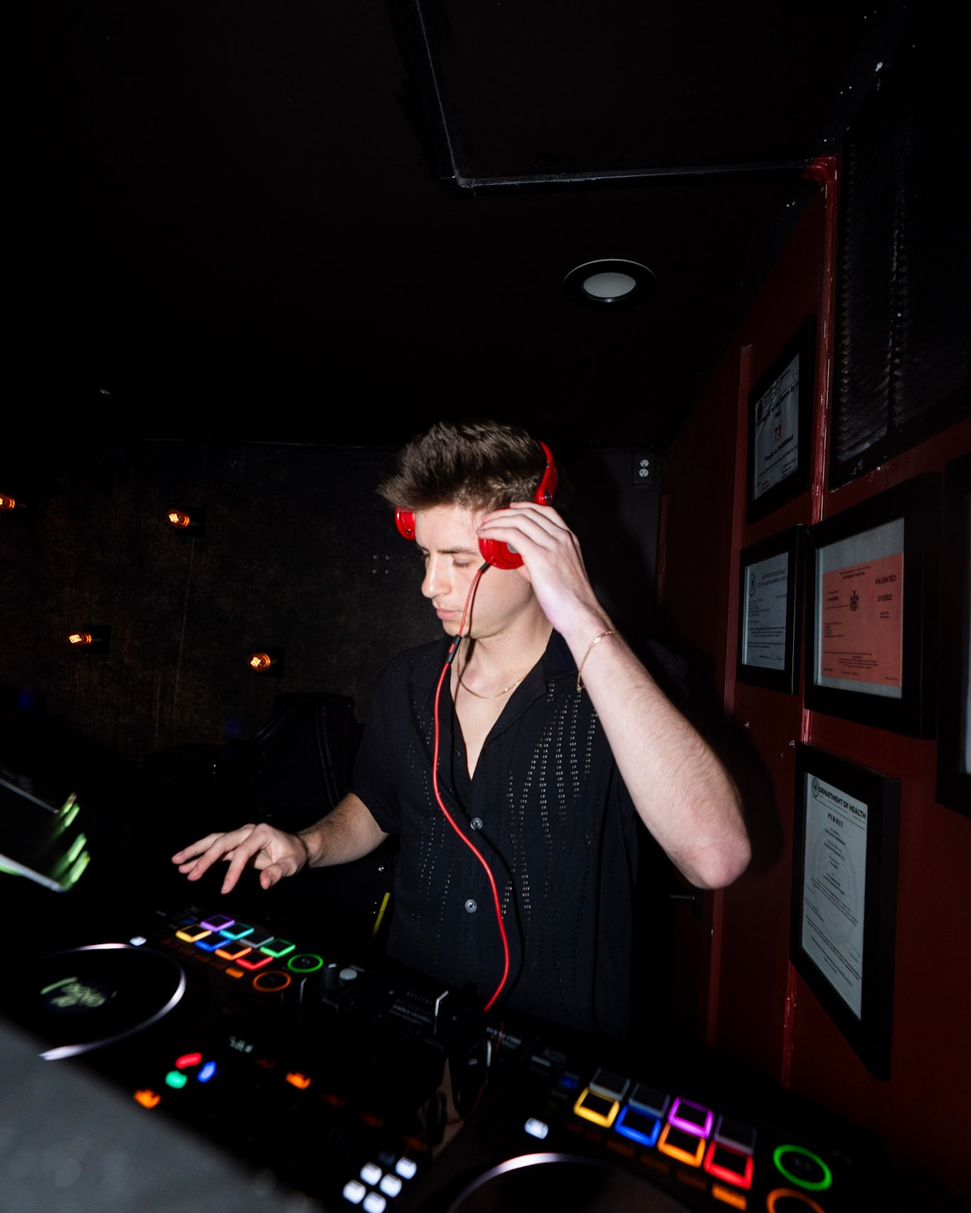 DJ Chris G mixing with red headphones in a dark nightclub DJ booth