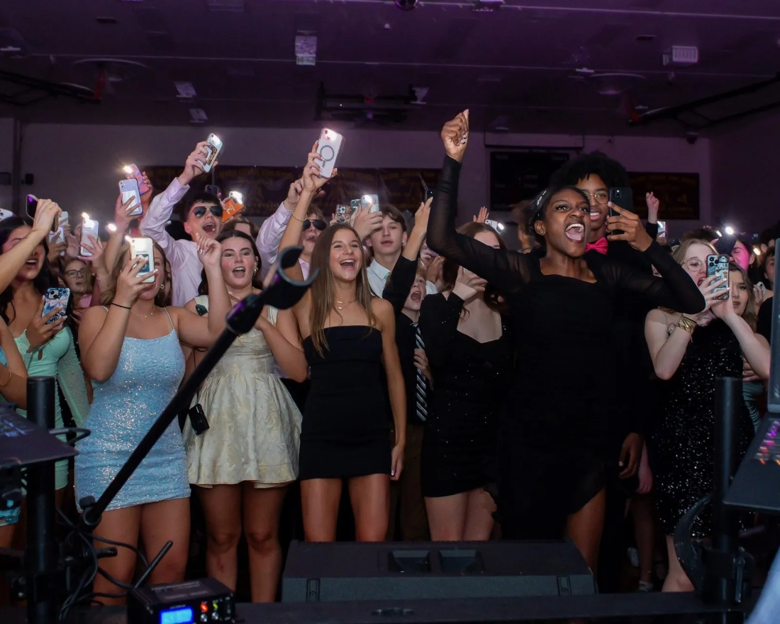 Students cheering with phone lights up in front of the DJ booth at a school dance